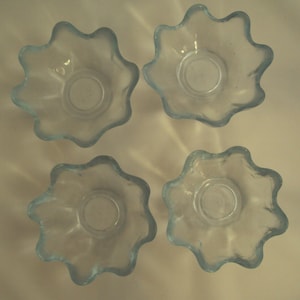 May include: Four light blue glass bowls with a wavy, scalloped edge. The bowls are empty and arranged in a square pattern.