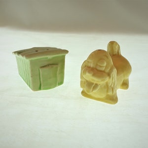 May include: A set of ceramic salt and pepper shakers shaped like a dog house and a dog. The dog house is green and the dog is yellow.