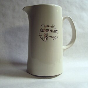 May include: White ceramic pitcher with a gold Schenley logo and a black cursive script.