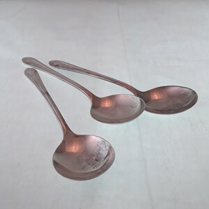 May include: Three silver serving spoons with rounded bowls. The spoons are arranged in a row, with the handles pointing in different directions.