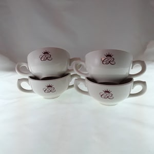 May include: Set of six white ceramic soup cups with two handles. Each cup has a burgundy crown and the letters "CR" printed on the front.