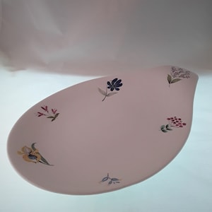 May include: A white oval serving platter with a floral design. The platter features a variety of flowers in shades of blue, pink, yellow, and green.
