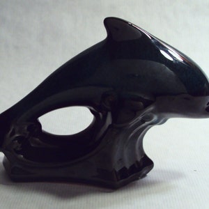 May include: A black ceramic dolphin figurine with a glossy finish. The dolphin is leaping out of the water, with its tail and body forming a ring.