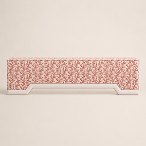 May include: A rectangular bench featuring a white base with a repeating coral-colored branch pattern across the upholstery. The bench has a low profile with a distinct cutout design at the bottom of each side, creating four short, sturdy feet.