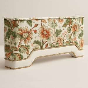 Op de afbeelding: Een rechthoofd met een bloemenpatroon in tinten oranje, groen en crème. Het hoofdbord heeft een witte basis met gouden rand. Het bloemenpatroon heeft grote bloemen en bladeren.