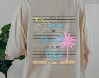 May include: A cream-coloured t-shirt featuring a graphic on the back. The design incorporates a yellow aeroplane, a heart-shaped dotted line, and the words "I AM THE WAY THE TRUTH AND THE LIFE" in blue and pink, with "JOHN 14:6" at the bottom.