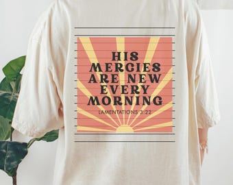 May include: Cream-coloured t-shirt with a graphic on the back. The graphic features the text "HIS MERCIES ARE NEW EVERY MORNING" in black, set against a rising sun design in orange and yellow. The text "LAMENTATIONS 3:22" is below.