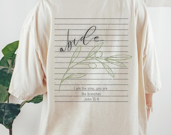 May include: Off-white t-shirt with a back graphic. The design includes the word "abide" in cursive, an olive branch illustration, and the text "I am the vine, you are the branches John 15:4" within a rectangular frame.