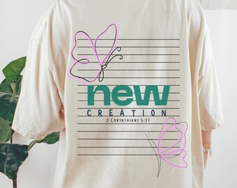 May include: Cream-coloured t-shirt with a graphic on the back. The graphic includes the word "new" in teal, the word "creation" in white, and the Bible verse "2 Corinthians 5:17". Two pink butterfly outlines are also featured.