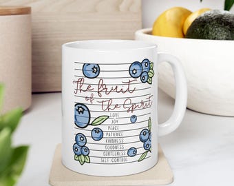 May include: White ceramic mug with the text "The Fruit of the Spirit" and blueberry illustrations. The mug lists virtues including love, joy, and peace. The design is in a handwritten style.