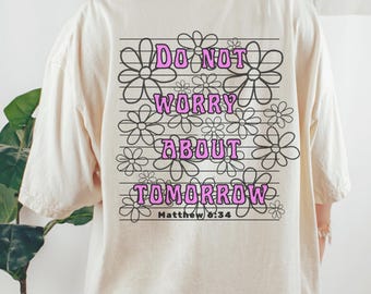 May include: Cream-coloured t-shirt with a floral design and the text "DO NOT WORRY ABOUT TOMORROW" in pink, with the Bible verse Matthew 6:34. The design features daisy-like flowers.