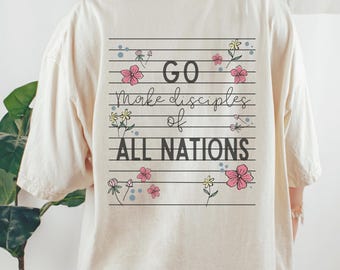 May include: Cream-coloured t-shirt featuring the text "GO make disciples of ALL NATIONS" in black, adorned with pink and yellow floral designs. The shirt has a loose fit and short sleeves.