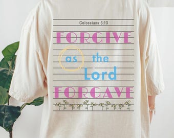 May include: Cream-coloured t-shirt with the text "FORGIVE as the Lord FORGAVE" in pink and blue, with a yellow circle around the word "as". The text is on a lined background, with small flower graphics at the bottom. The text "Colossians 3:13" is at the top.