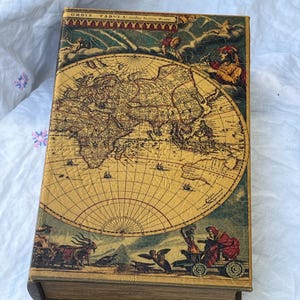 May include: A vintage-style book with a world map design. The cover features a detailed illustration of the globe with historical figures and text. The book has a worn, antique appearance, with a tan and brown color scheme.