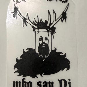 Può includere: Un adesivo in vinile nero con un'illustrazione stilizzata di una figura barbuta che indossa un elmo a secchio con grandi corna. Il testo "The Knights" è arcuato sopra la figura e "who say Ni" è stampato in nero sotto il grafico.