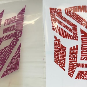 May include: Two die-cut vinyl decals featuring the Transformers logo. One is purple with Decepticon characters, the other is red with Autobot characters. Each logo is filled with character names.