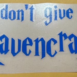 Può includere: Adesivo in vinile blu con la frase "I don't give a Raven crap" in un font gotico. L'adesivo è su un supporto trasparente, con uno sfondo giallo.