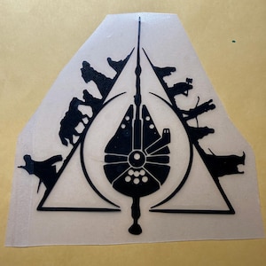 Op de afbeelding: Zwarte afbeelding van het ruimteschip Millennium Falcon in een driehoek, met silhouetten van personages en schepen eromheen. Het ontwerp staat op een transparante sticker.