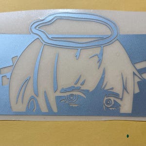 May include: A light blue sticker featuring a stylized anime-style character with a halo and Japanese text. The character's face and hair are visible, with the eyes as a focal point. The design is cut out.