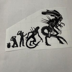May include: A black vinyl decal featuring an evolutionary sequence of the Xenomorph creature. The design progresses from an egg to a facehugger, a human host, a chestburster, and finally a large, fully developed adult alien with a tail.
