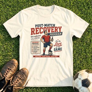 Könnte beinhalten: Ein cremefarbenes Kurzarm-T-Shirt mit einer Grafik eines Fußballspielers mit Flasche und Ball. Der Text lautet: POST-MATCH RECOVERY PROGRAM, Not professional. STILL EFFECTIVE., RECOVERY PROTOCOL, For the Love OF THE GAME, GOOD GAME. GOOD FRIENDS. GOOD TIMES.
