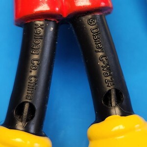 May include: Close-up of a toy figure's legs. The legs are black with yellow shoes and red shorts. The text "Kellogg Co. China" and "&copy; Disney C-WB 24" are visible on the legs.
