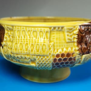May include: A yellow ceramic bowl with a pedestal base. The bowl features a textured design with brown and yellow patterns. The bowl is likely for decorative or functional use.