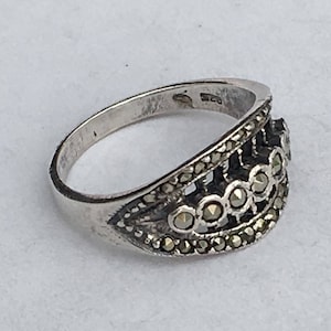 May include: A silver ring with a decorative design. The ring features small, round stones set in a detailed pattern. The band is smooth and polished, and the overall design is intricate and elegant.