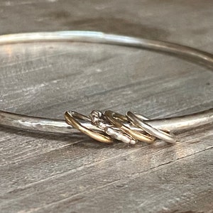 May include: A silver bangle bracelet with a hammered finish and a cluster of five smaller rings, some gold and some silver, attached to it.