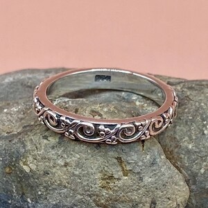 May include: A silver band ring with a delicate, intricate design of swirls and dots around the entire band.