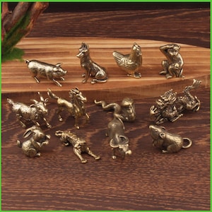 Könnte beinhalten: Eine Sammlung kleiner Tierfiguren in Bronzeoptik, darunter ein Schwein, ein Hund, ein Huhn, ein Affe, eine Ziege, ein Pferd, eine Schlange, ein Drache, ein Kaninchen, ein Tiger, ein Bulle und eine Ratte. Auf Holzgrund.
