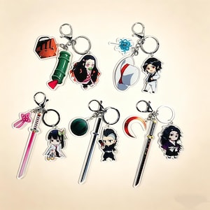 May include: Collection of anime-themed keychains featuring various characters and objects. Keychains include a red bag, a green bamboo tube, a white hat, a sword, and a crescent blade. Each keychain has a silver ring.