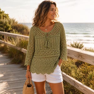 Pode incluir: Uma blusa de crochê verde-sálvia com decote redondo, fecho de cordão com borlas, mangas três quartos e bainha recortada, combinada com calções brancos lisos e uma mala de mão em palha entrançada.