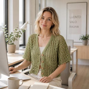 May include: A sage green crochet cardigan featuring a V-neckline, short sleeves, and a front button closure with four light brown wooden buttons. The garment has an open-knit square pattern throughout and is worn over a plain white top.