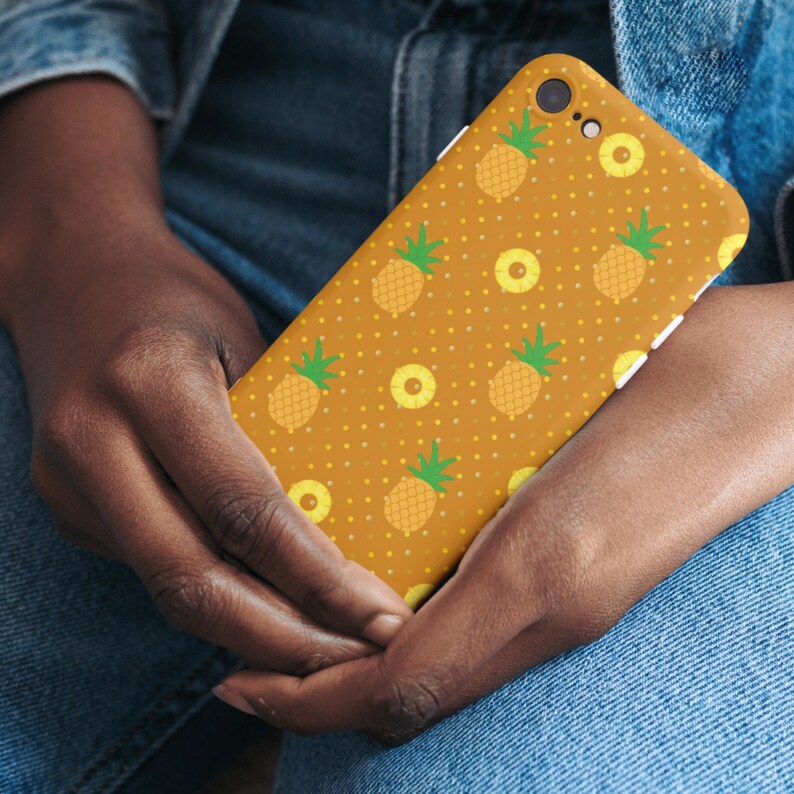 Op de afbeelding: Een smartphonehoesje met een mosterdgele achtergrond en een herhalend patroon van kleine ananassen en ananasringen, geaccentueerd door een subtiel wit stippenontwerp over het gehele oppervlak van de beschermhoes.