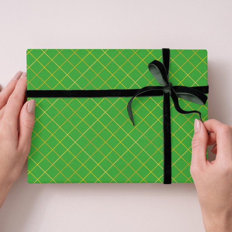 Op de afbeelding: Een rechthoekige geschenkdoos verpakt in felgroen papier met een gouden diagonaal ruitpatroon. De doos is gestrikt met een zwart fluwelen lint dat aan de rechterkant tot een strik is geknoopt, wat een contrast vormt met het groen en goud.