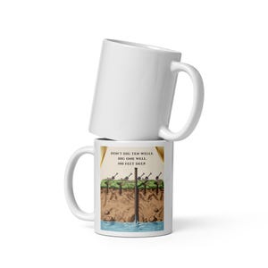 Op de afbeelding: Twee witte keramische mokken verticaal op elkaar gestapeld. De onderste mok heeft een grafische illustratie van een diepe put met de tekst: DON'T DIG TEN WELLS. DIG ONE WELL. 100 FEET DEEP. De afbeelding toont schoppen boven een waterbron.