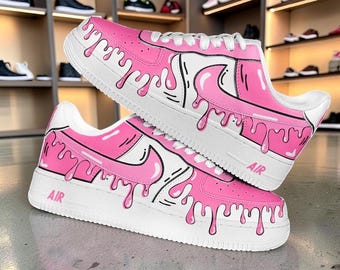 May include: A pair of pink and white sneakers with a unique drip design. The shoes feature a white sole, pink uppers, and a black outline. The word "AIR" is printed on the side of the sole. The sneakers are displayed on top of each other.