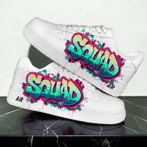 Puede incluir: Zapatillas blancas con la palabra "SQUAD" en estilo grafiti, con tonos turquesa, rosa y amarillo. Las zapatillas tienen el texto "AIR" cerca de la suela.