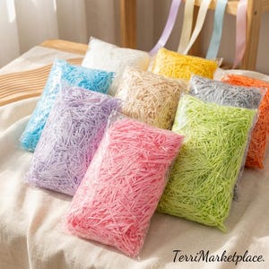 Può includere: Una collezione di carta sminuzzata colorata in sacchetti di plastica trasparente. I colori includono rosa, verde, viola, blu, giallo, bianco, beige, grigio e arancione. Nastri di vari colori sullo sfondo. Il testo "TerriMarketplace" è in basso a destra.