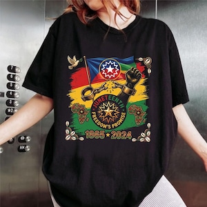 Op de afbeelding: Zwart T-shirt met een kleurrijke afbeelding ter viering van Juneteenth. Het ontwerp bevat een vlag, een vuist, de tekst "Juneteenth Freedom's Promise 1865-2024" en de omtrek van het Afrikaanse continent. Er is ook een duif met een olijftak afgebeeld.