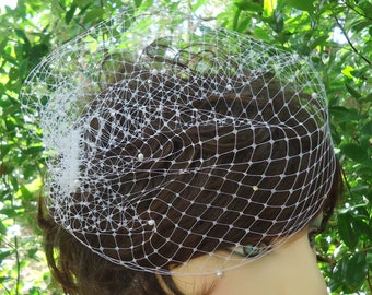 May include: White birdcage veil with pearl embellishments. The veil is made of a fine mesh material and has a delicate, romantic look.