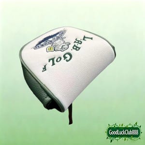 Könnte beinhalten: Ein weiß-grüner Putter-Schlägerhaube mit dem in Dunkelgrün gestickten Text L.A.B. GOLF. Das Design enthält eine kleine gestickte Grafik einer Zeichentrickfigur, die einen Hut trägt und ein gelbes quadratisches Objekt auf einer blauen Basis hält.