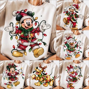 Peut inclure: Un sweat-shirt à col rond couleur crème avec une impression graphique de Mickey Mouse vêtu d'un costume de Père Noël, entouré de guirlandes lumineuses colorées. Le design présente des variantes avec Dingo, Donald, Minnie, Pluto et Daisy, chacun portant une tenue de fête et emmêlé dans des guirlandes lumineuses.