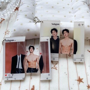 May include: Two rectangular acrylic keychains featuring Instagram-style frames. One shows a person in a black suit and a shirtless person with defined abs. The other shows a person in a black hoodie and a shirtless person. Both include metal chains.