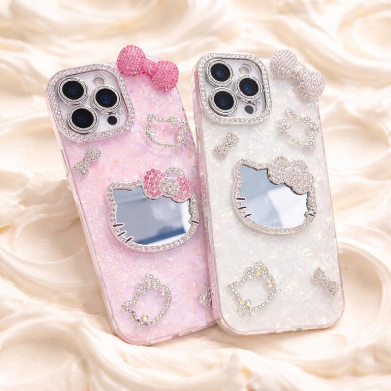 May include: Two bedazzled phone cases. One is pink with a pink bow and a Hello Kitty mirror. The other is white with a silver bow and a Hello Kitty mirror. Both cases have silver rhinestone accents.