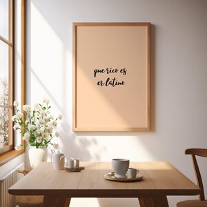 Peut inclure: Une affiche encadrée avec le texte "que rico es er latino" en écriture noire. L'affiche a un fond couleur pêche et un cadre en bois. L'affiche est accrochée sur un mur blanc au-dessus d'une table en bois.