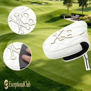 May include: A white golf putter headcover featuring a quilted diamond pattern and an embroidered skull and crossbones design. The cover has a textured white exterior with a black interior lining and a metallic silver shaft attachment point.