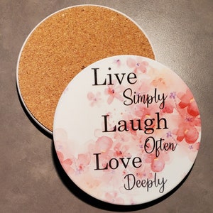 Puede incluir: Posavasos redondo de cerámica con fondo blanco y diseño floral de acuarela rosa. El posavasos presenta el texto "Live Simply Laugh Often Love Deeply".