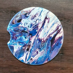 May include: A round coaster with a blue, white, and purple abstract swirl design. The coaster is made of a hard, durable material and is perfect for protecting surfaces from spills.